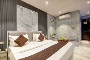 A modern hotel room with a large bed, marble-patterned walls, a built-in bench, and a small table with amenities. - Hotel Heritage Home (New Delhi)