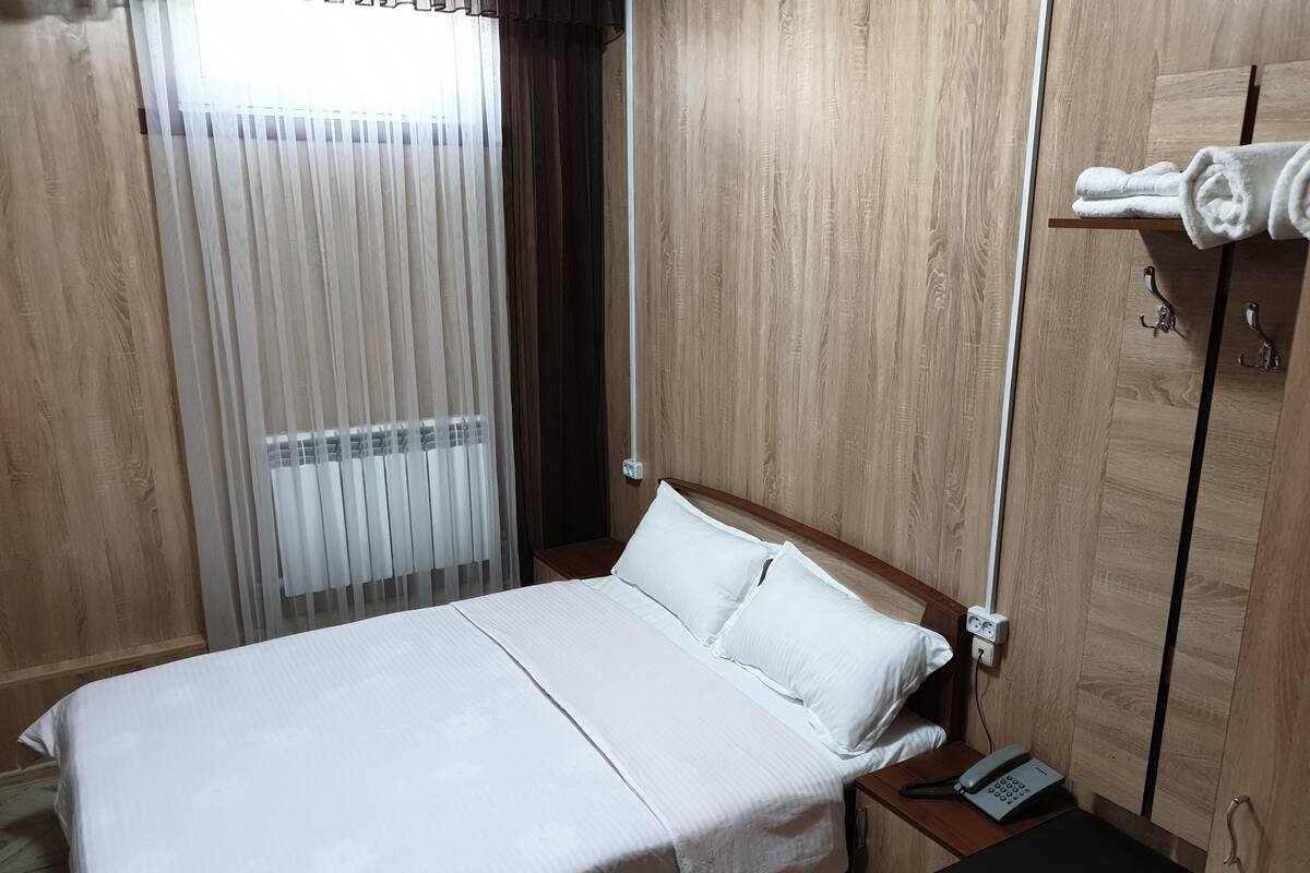 A hotel room with a wooden bed, white bedding, a bedside phone, and a small wooden nightstand.
