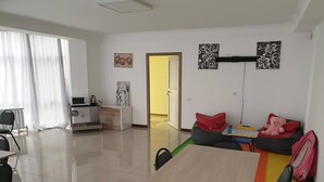 A spacious living room with a dining area, a sofa with toys, and a kitchen in the background. - Bal-Meyir Hotel Almaty (Almaty)