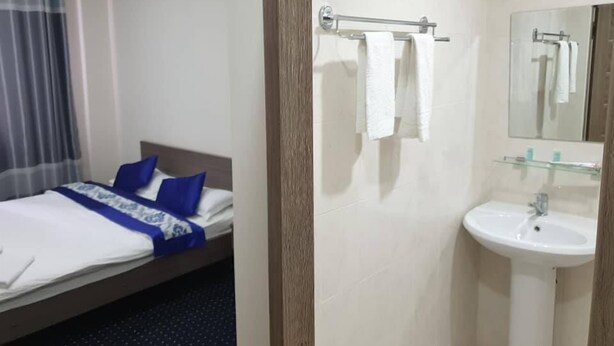 A hotel room with a bed, a bathroom with a sink and mirror, and a window with curtains. - Bal-Meyir Hotel Almaty (Almaty)