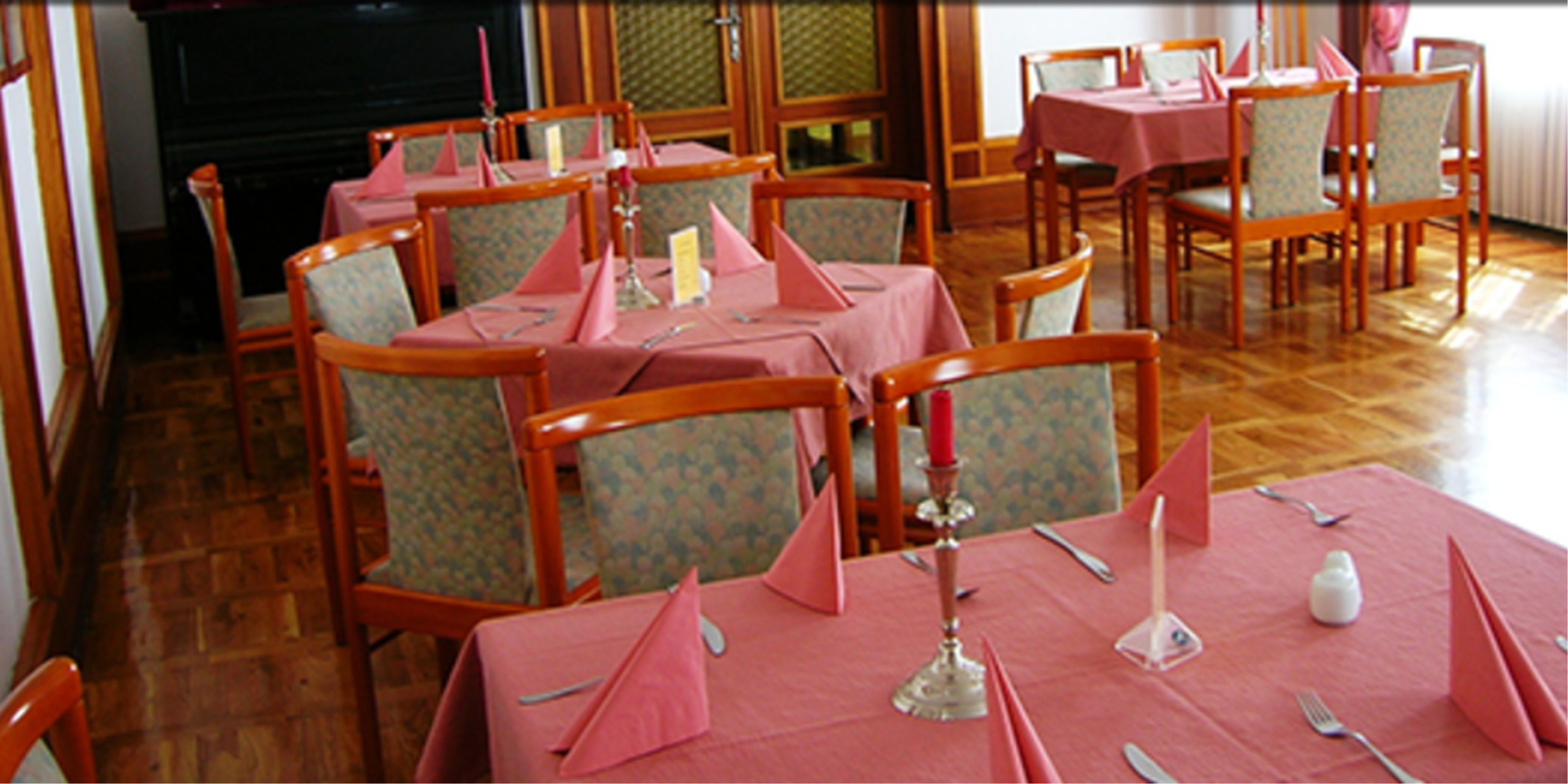 Ein Essbereich mit Tischen für vier Personen, jeder Tisch ist mit einer rosa Tischdecke und Besteck gedeckt, dazu gehören stuhlähnliche Sitzgelegenheiten mit Blumenmuster.