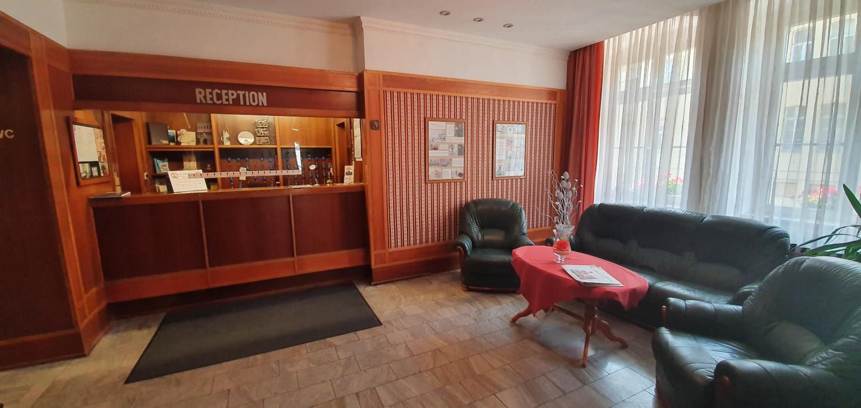 A reception area with a wooden reception desk, a black leather chair, a red table, and a black leather sofa.