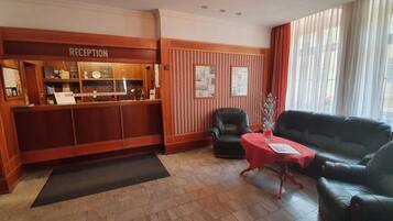 A reception area with a wooden reception desk, a black leather chair, a red table, and a black leather sofa.