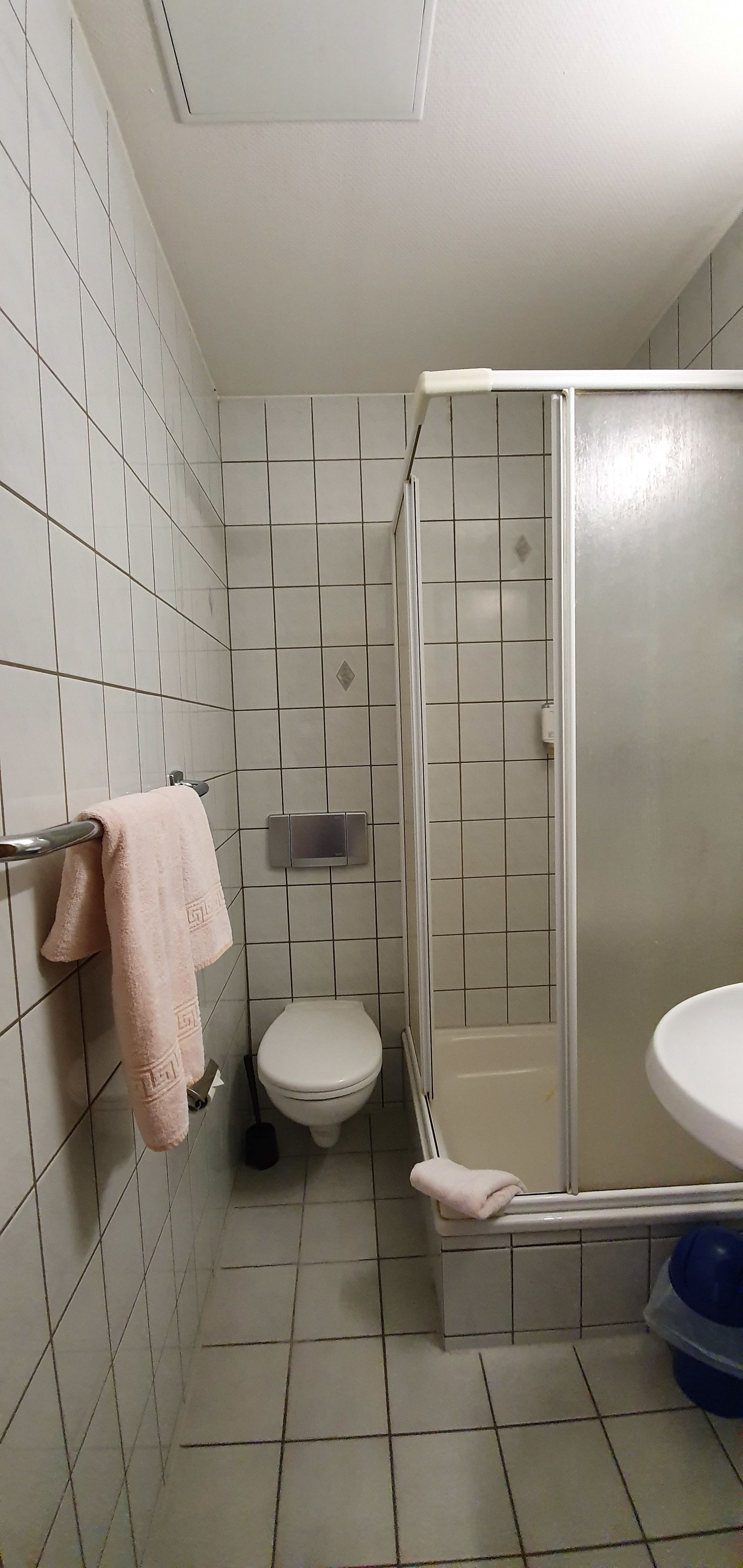 A bathroom with white tiled walls, a toilet, a shower enclosure, and a sink.