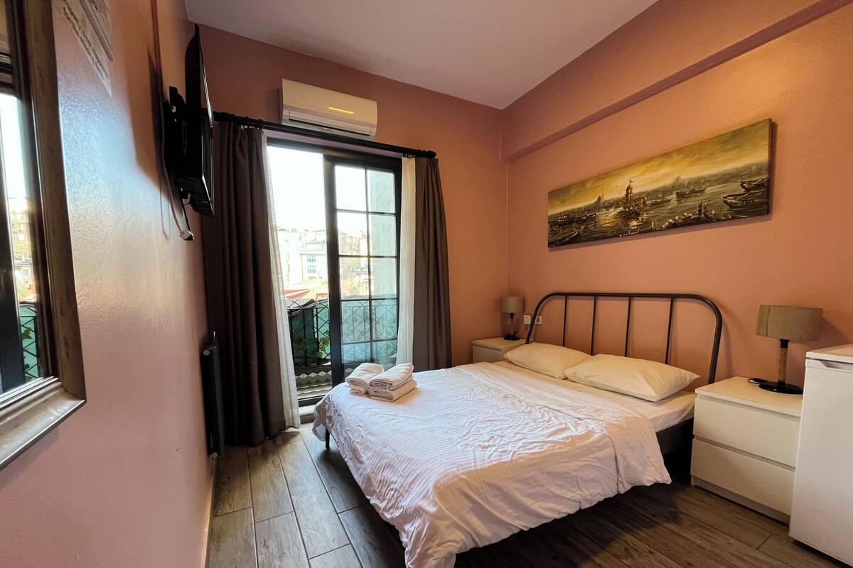Habitación de hotel con cama, mesitas de noche, un cuadro y vistas al exterior.