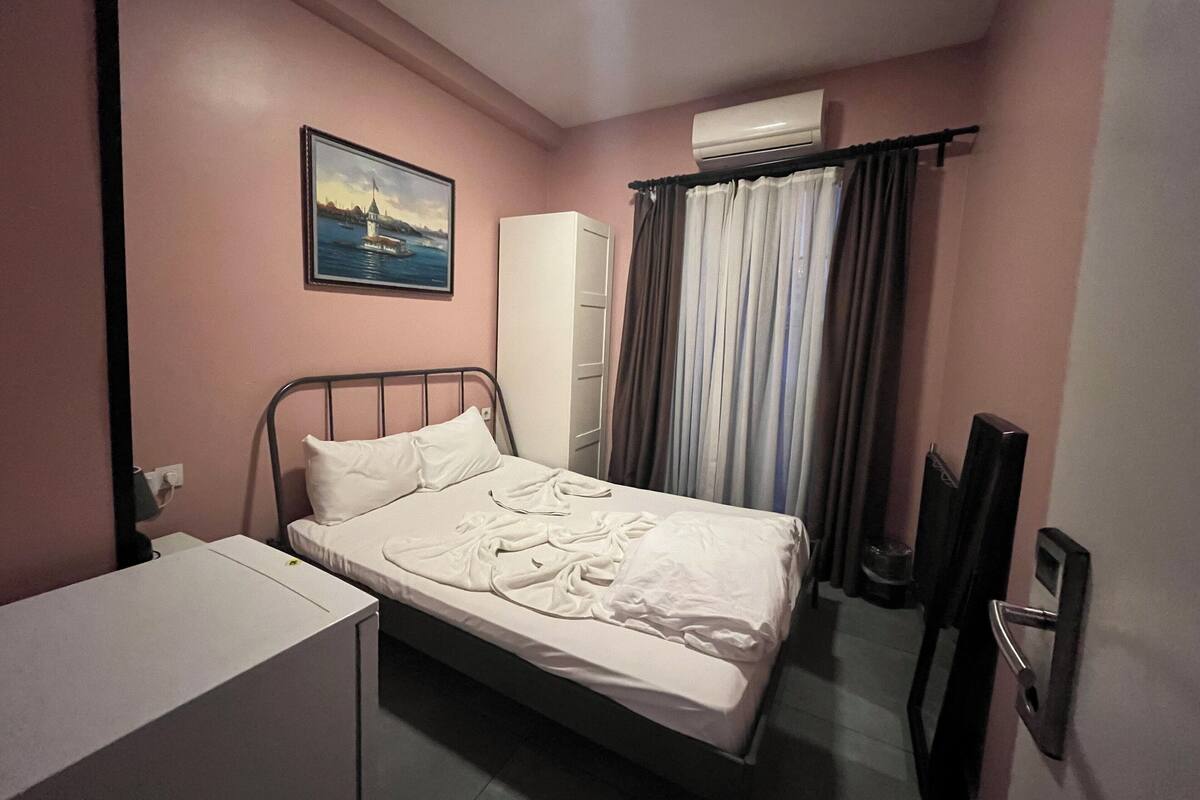 Un dormitorio con una cama, un escritorio, un armario, un cuadro y un equipo de aire acondicionado.