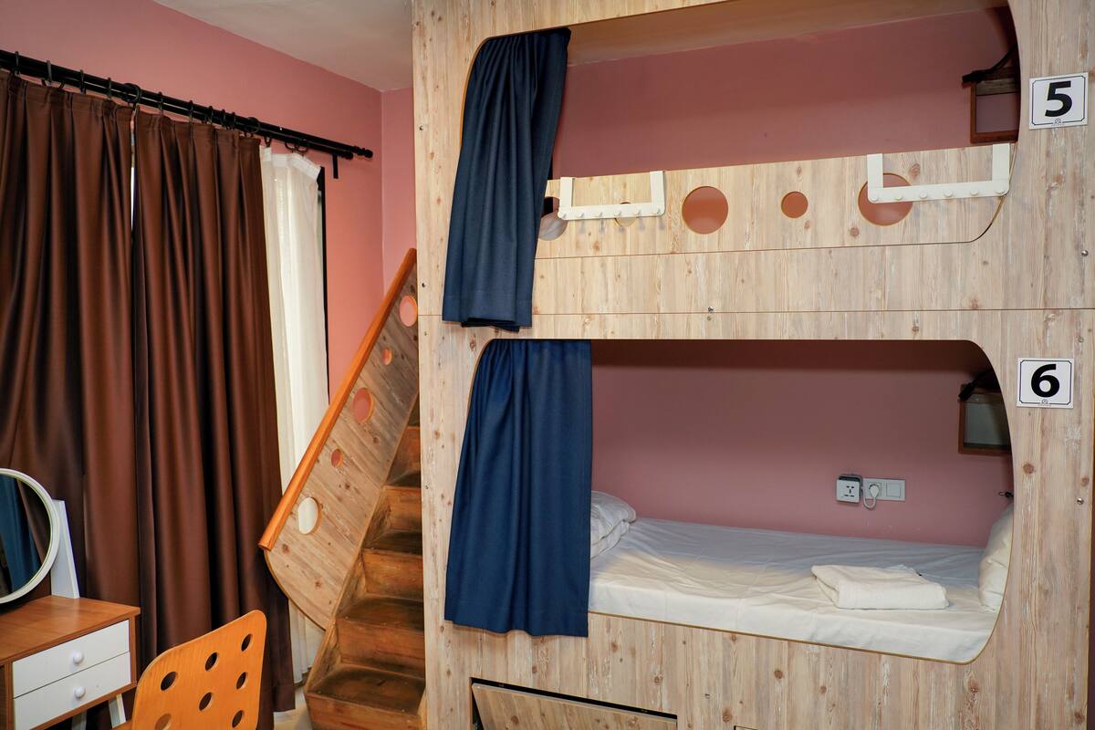 Habitación con literas de madera, un escritorio con espejo y una silla.