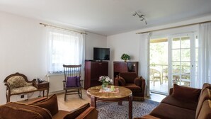 Una sala de estar con un sofá, una mesa de centro de madera, un televisor y vistas al exterior a través de un ventanal.