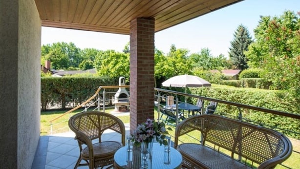 Un patio cubierto con muebles de mimbre, una mesa con un florero y una parrilla al fondo.