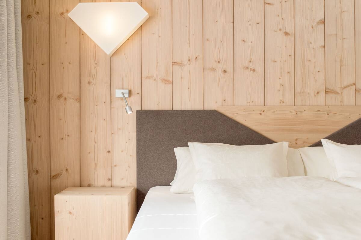 A hotel room with a wooden wall, a bed with white bedding, and a nightstand.