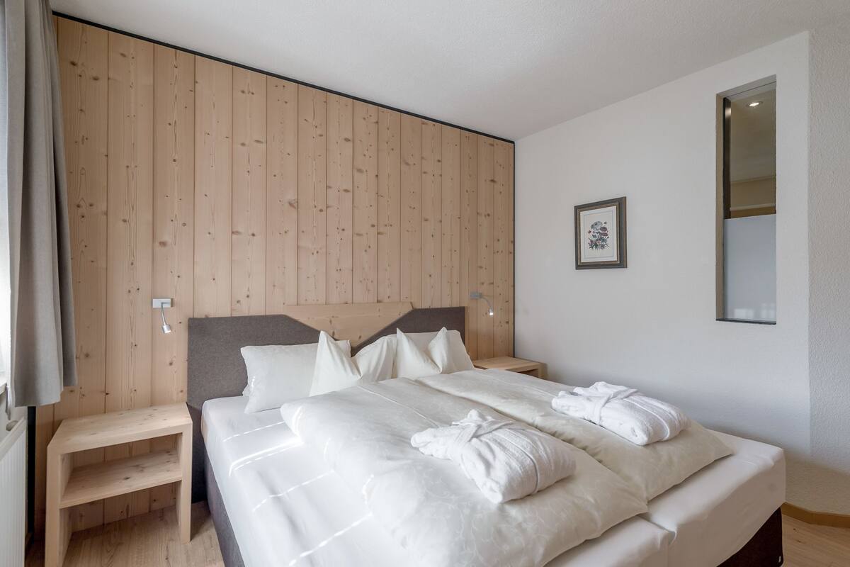 A bedroom with a wooden headboard, a bed with white linens, a bedside table, and a framed picture on the wall.