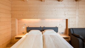Un dormitorio de cabaña de madera con dos camas, una mesita de noche, una silla y una lámpara fijada a la pared.