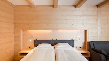 A wooden cabin bedroom with two beds, a nightstand, a chair, and a wall-mounted light fixture.