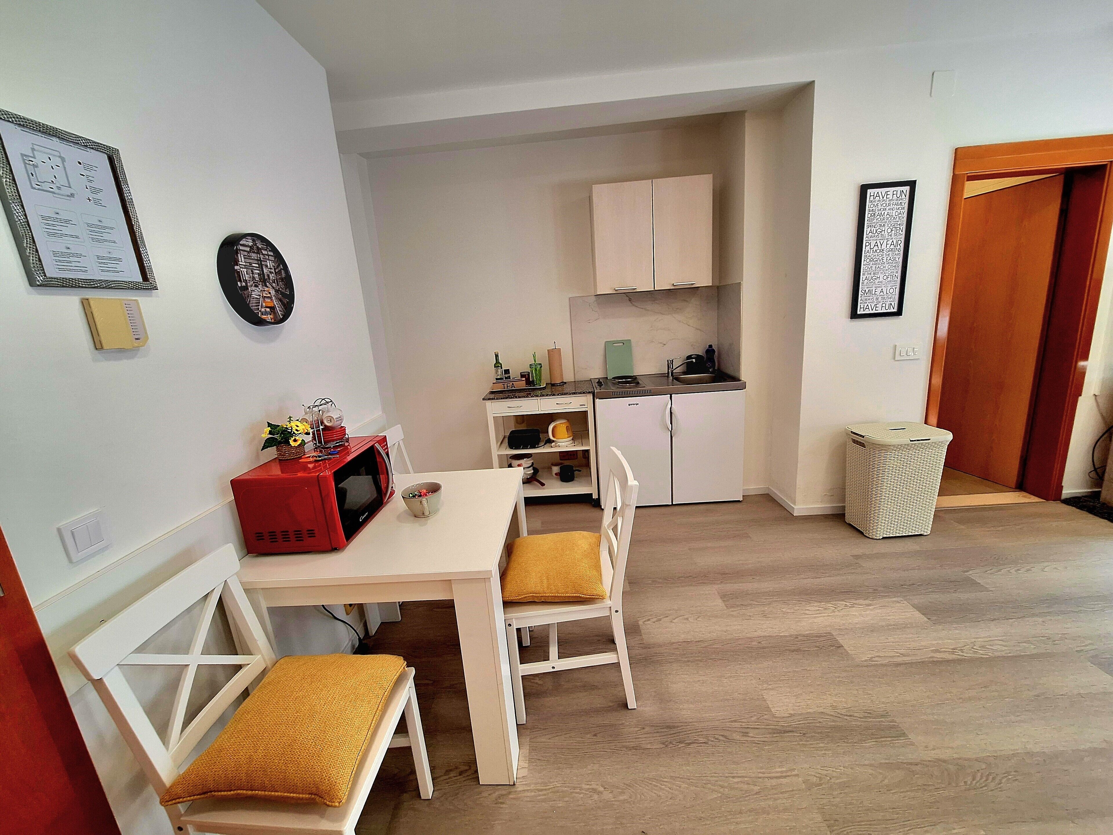 Cocina compacta con armarios blancos, microondas y un pequeño comedor con mesa y sillas.