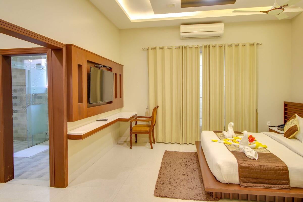 A hotel room with a bed, a desk, a chair, a TV, and a window with curtains.