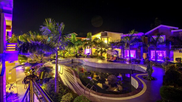 A nighttime view of a resort with a central pool, palm trees, and illuminated buildings. - Maulik Mansion Resort (Ramnagar)