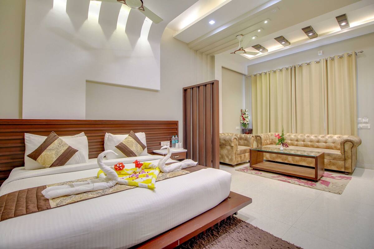 A hotel room with a large bed, a sofa, a coffee table, and a curtain.