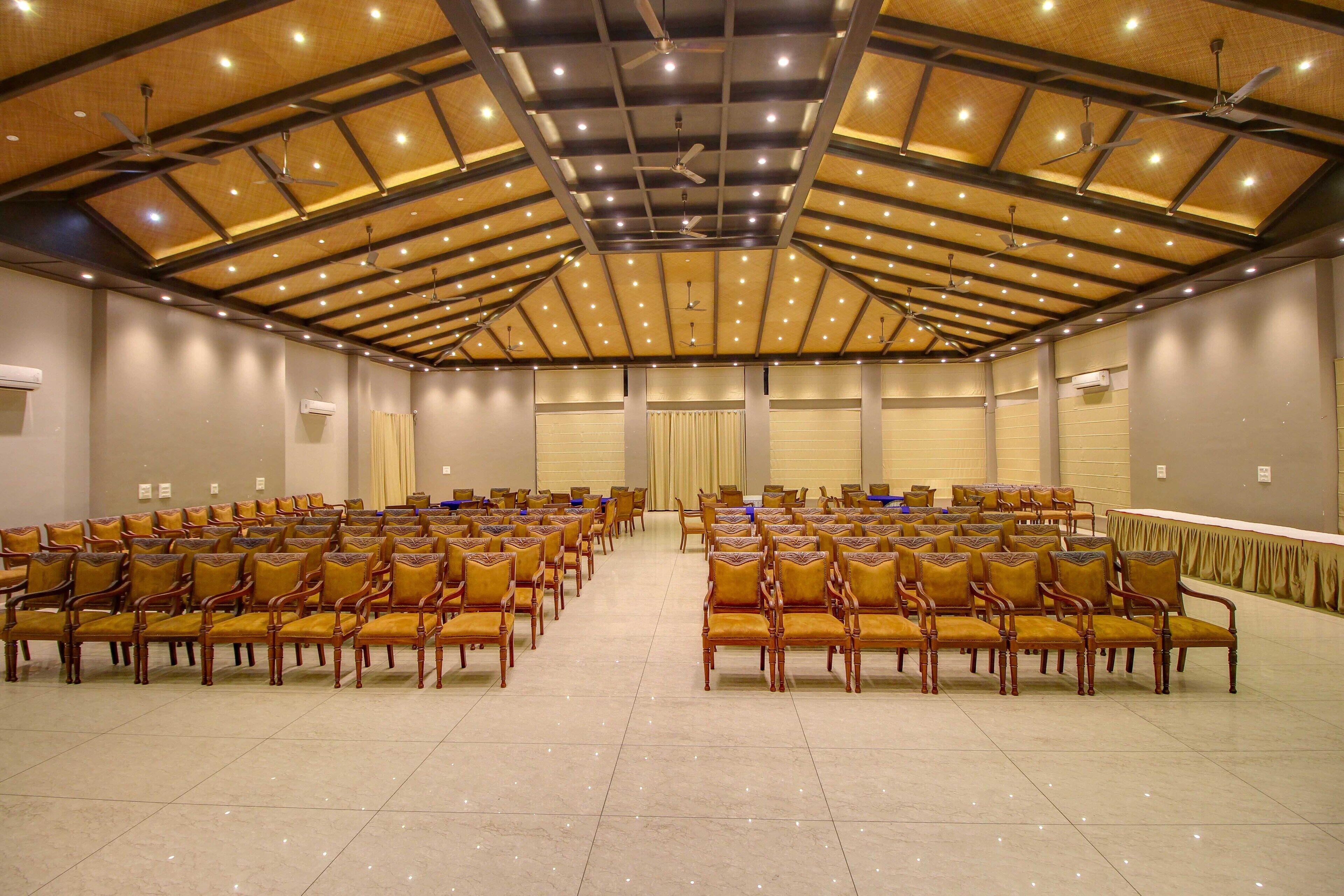 Ein großer Konferenzraum mit Reihen aus Holzstühlen und Deckenventilatoren.