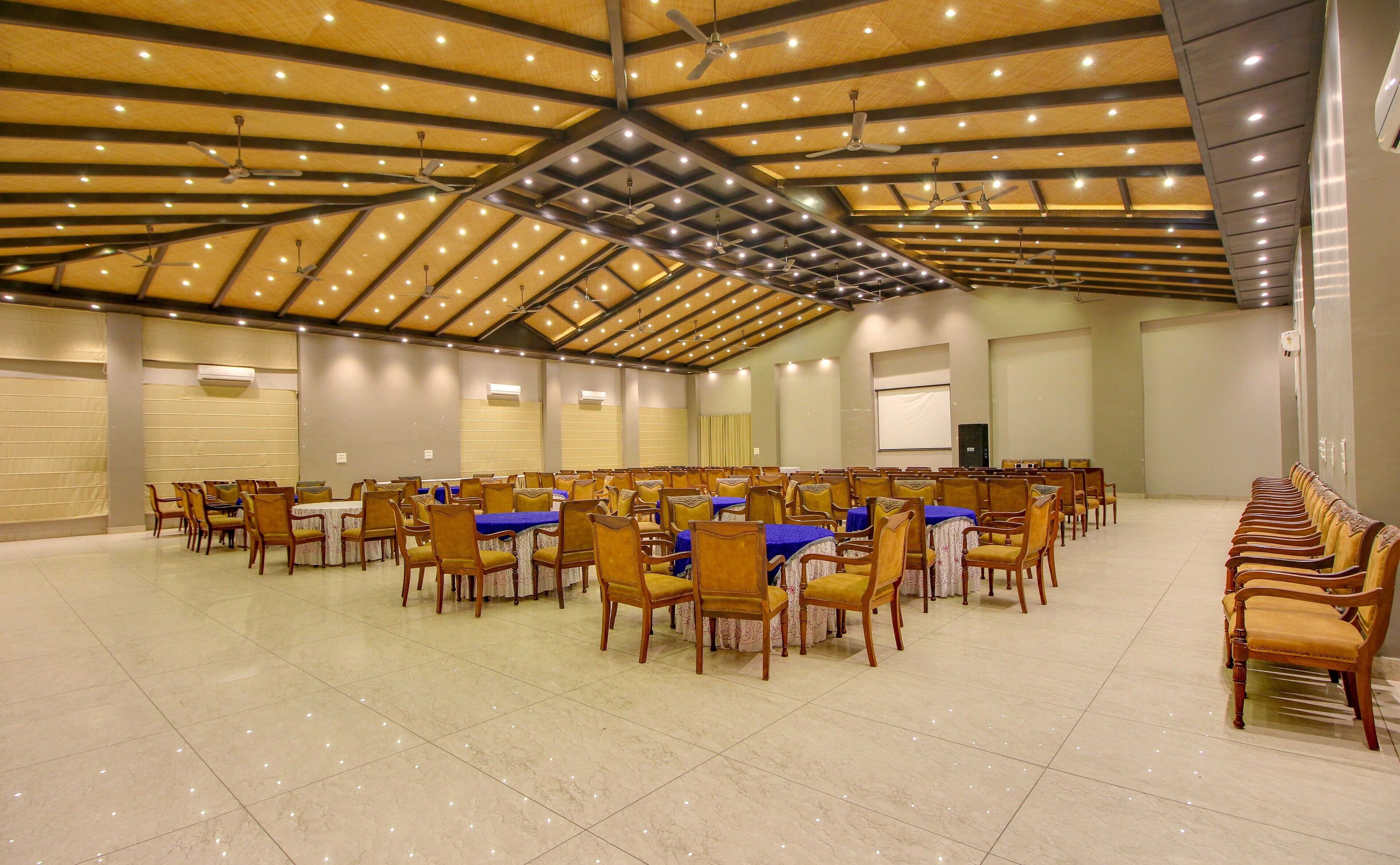 Un salón de conferencias amplio con filas de mesas y sillas, ventiladores de techo e iluminación empotrada.