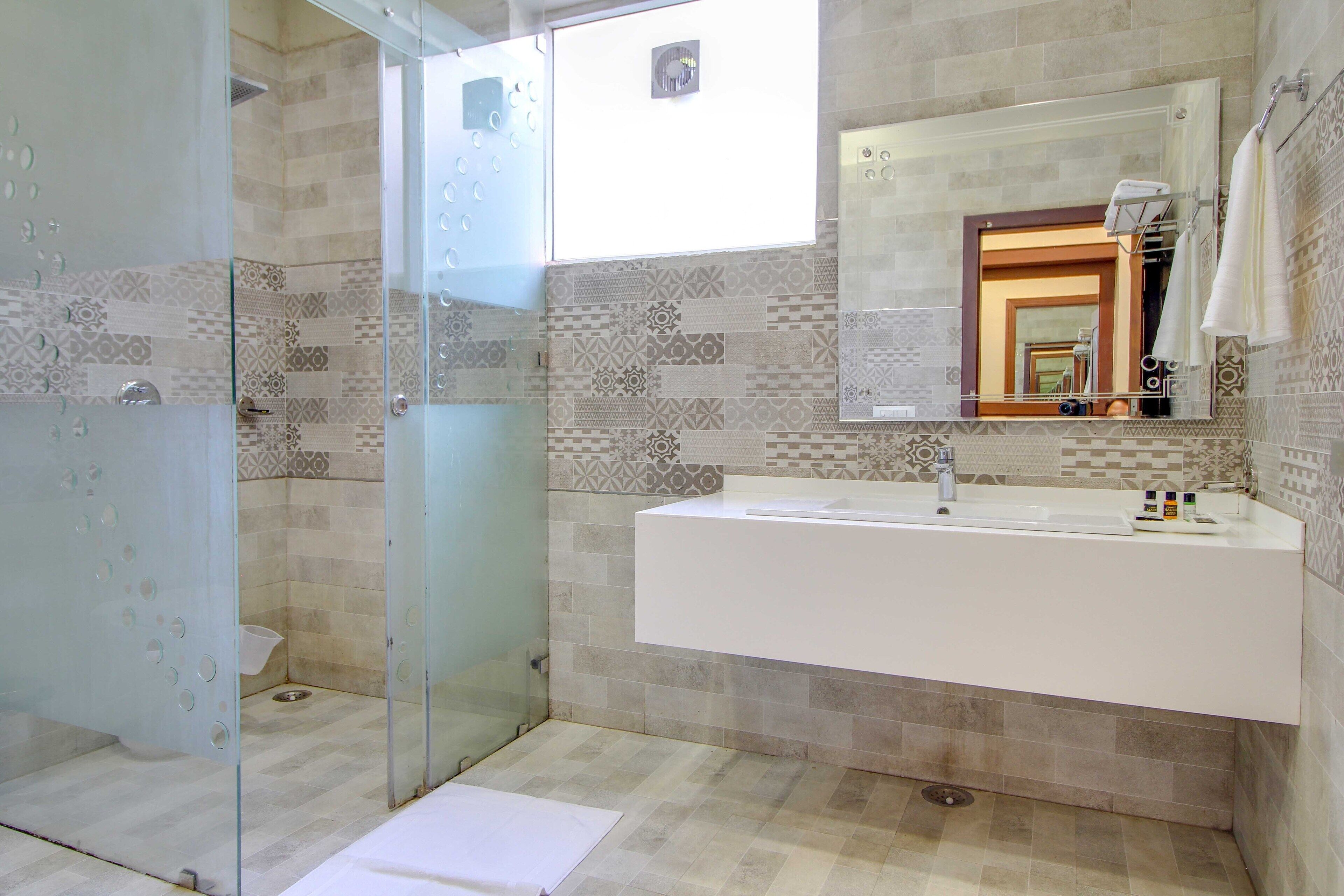 A modern bathroom with a glass shower enclosure, a large sink with a mirror, and patterned tiles on the walls.