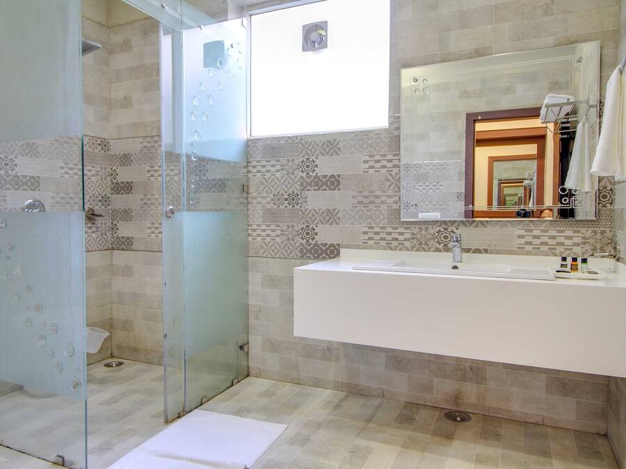 A modern bathroom with a glass shower enclosure, a large sink with a mirror, and patterned tiles on the walls.