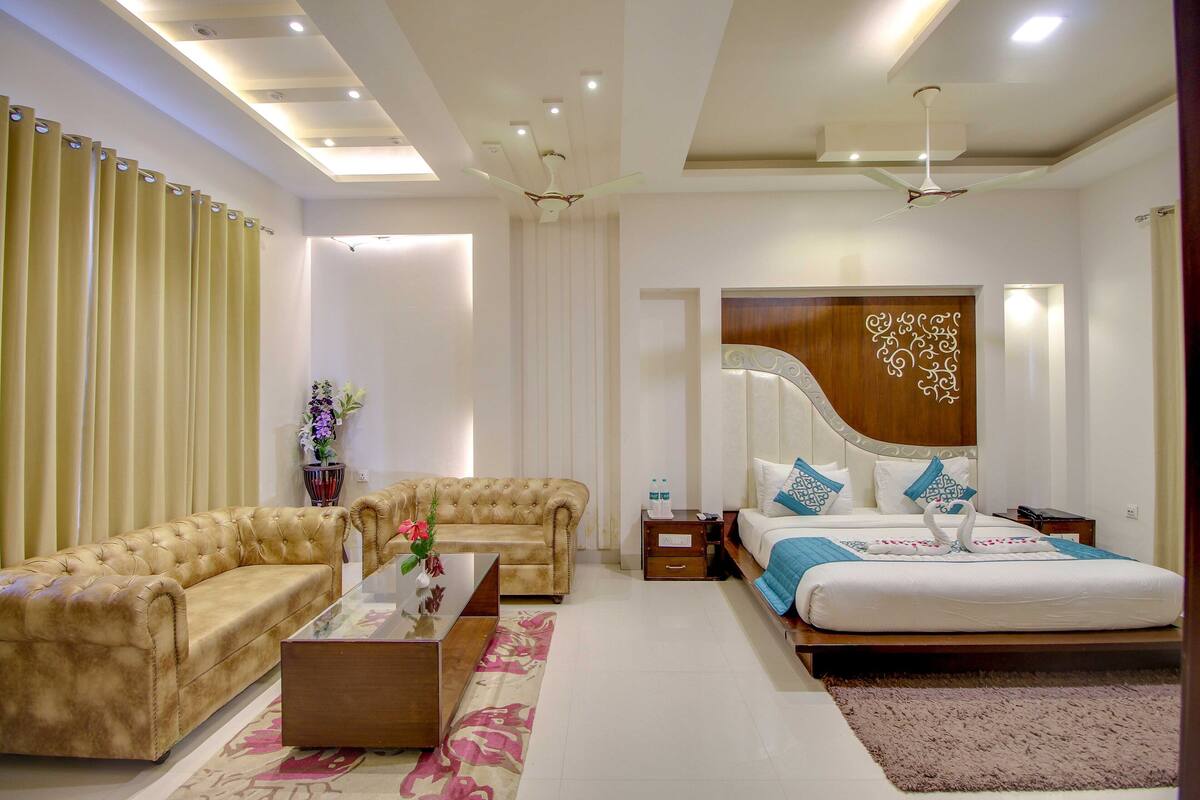 A modern hotel room with a large bed, a sofa, a coffee table, and a ceiling fan.