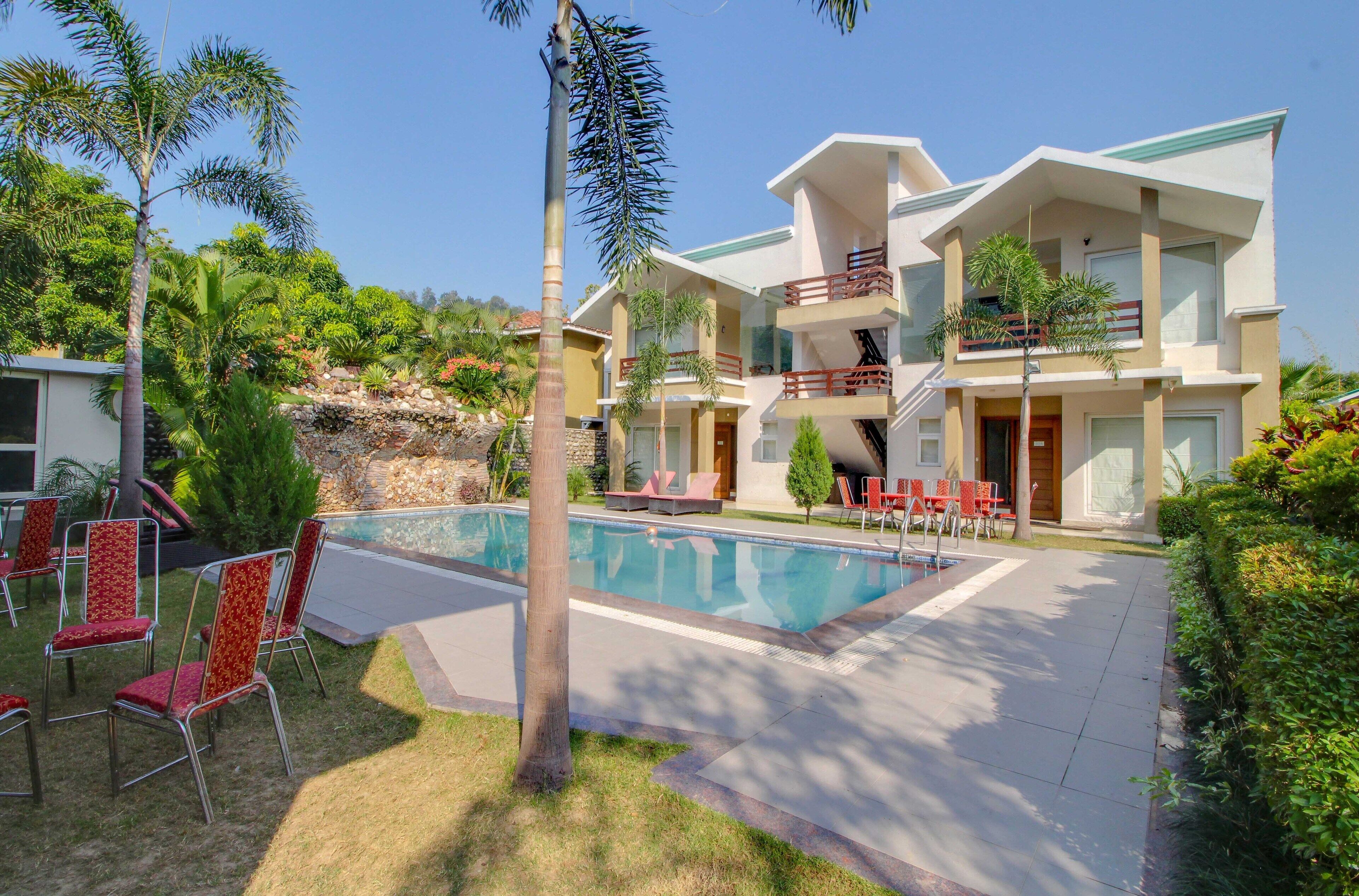 A two-story hotel with a swimming pool, outdoor seating, and lush landscaping.
