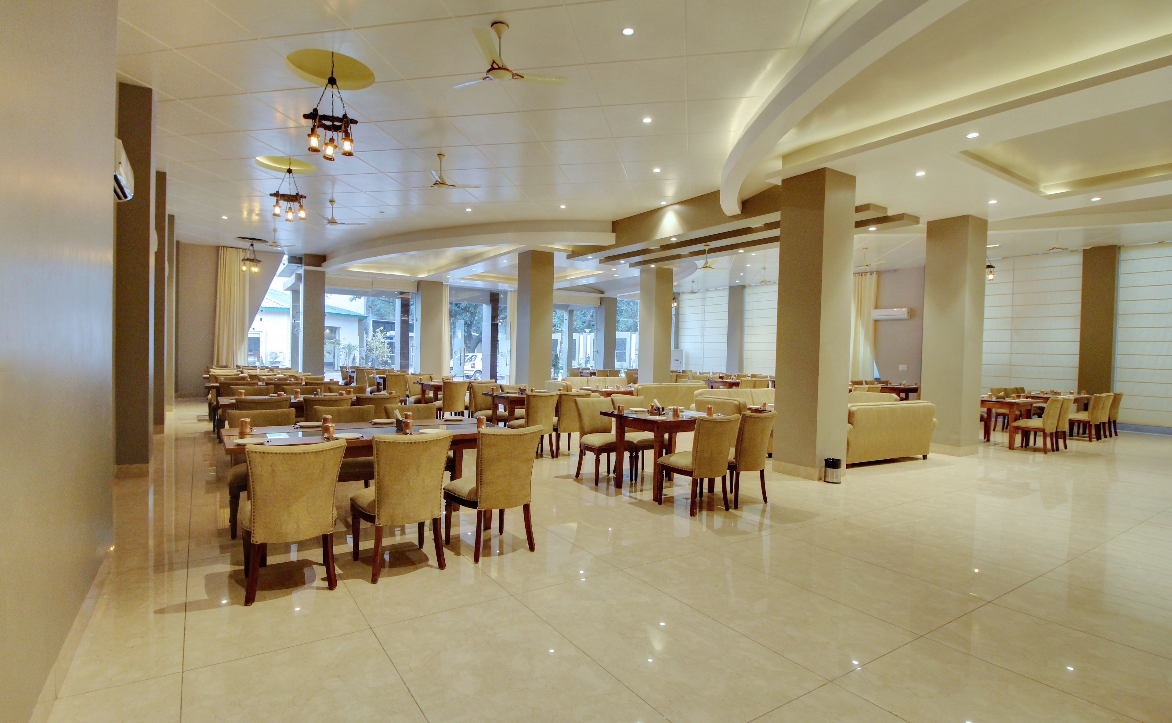 Amplia sala de desayunos de hotel con varias mesas y sillas, ventanas grandes y ventiladores de techo.
