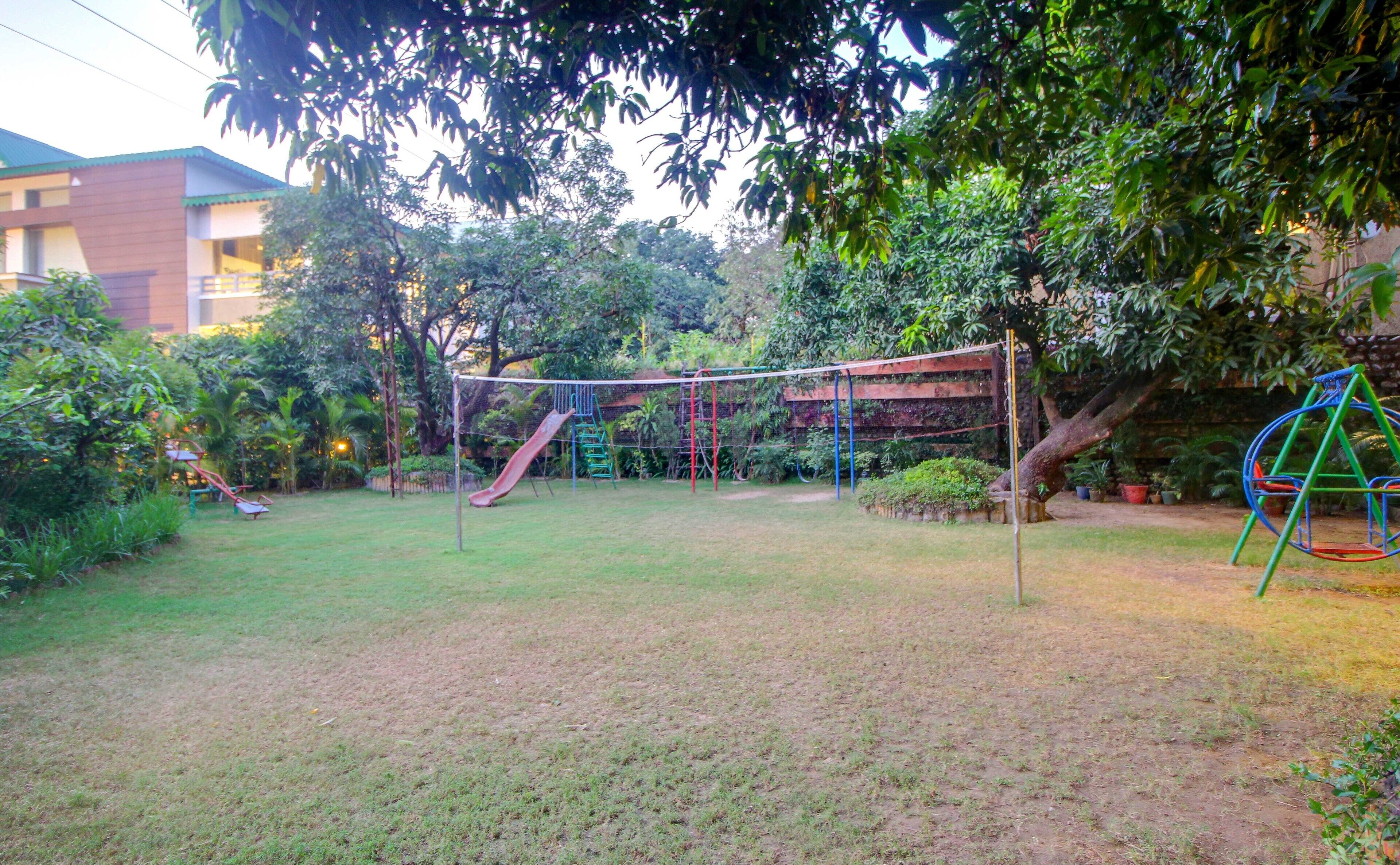 A playground with a slide and climbing structures, surrounded by trees and a building in the background.