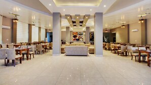 A spacious hotel lobby with multiple dining areas, a central seating area, and a ceiling with recessed lighting. - Maulik Mansion Resort (Ramnagar)