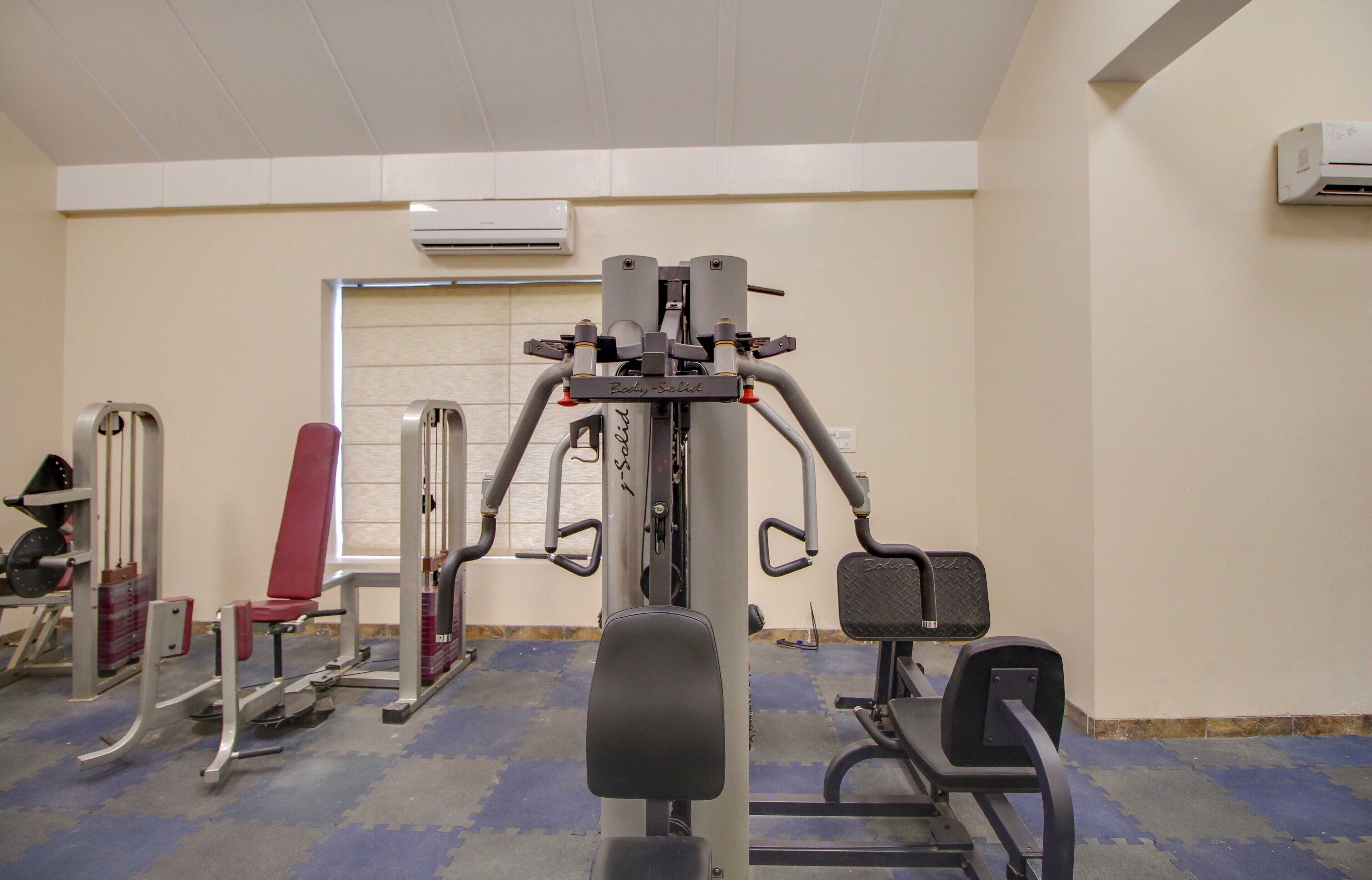 Un gimnasio con diferentes máquinas de ejercicio, una silla roja y una puerta al fondo.