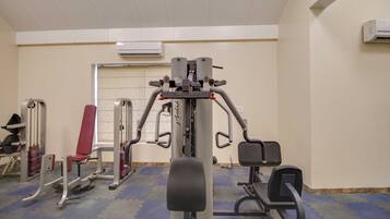 Un gimnasio con diferentes máquinas de ejercicio, una silla roja y una puerta al fondo.