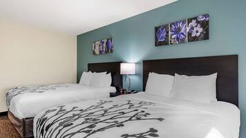 A hotel room with two beds, a nightstand, a lamp, and floral artwork on the walls.