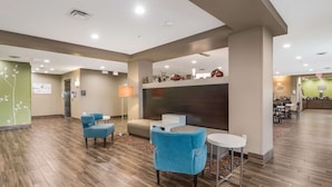 A spacious lobby with a modern design, featuring a seating area with blue chairs and a white table, a large dark-colored wall with decorative items, and a visible exit sign. - MainStay Suites at Discovery Park of America (Union City)