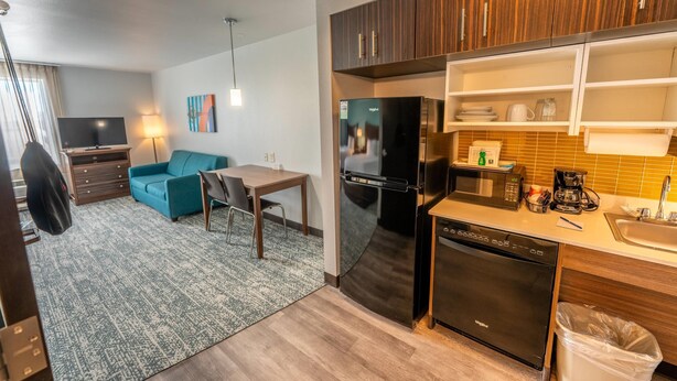 A modern kitchen with a refrigerator, microwave, and dishwasher. There is a dining area with a table and chairs, and a living room with a sofa and a TV. - MainStay Suites at Discovery Park of America (Union City)