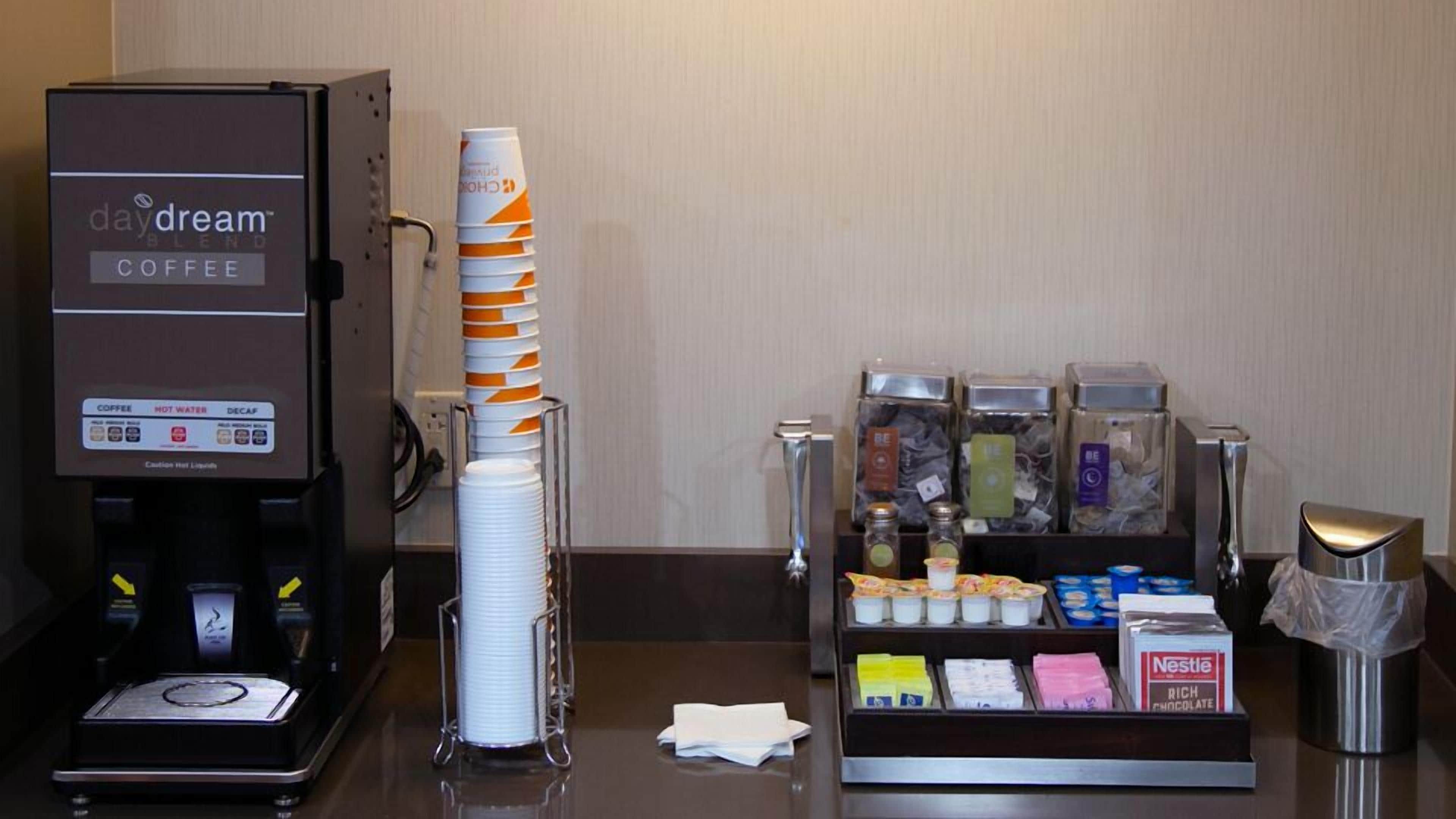 A coffee station with a coffee machine, disposable cups, and a variety of coffee pods and creamer options.