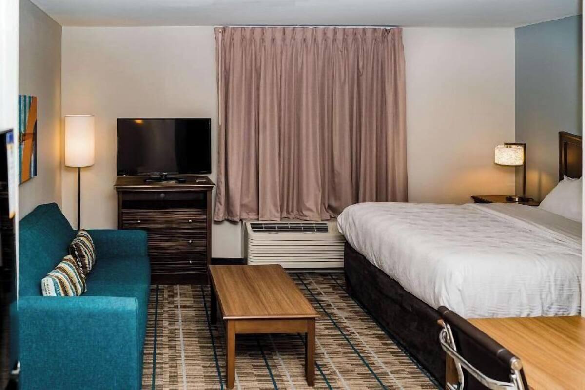 A hotel room with a bed, a sofa, a TV, a table, and a window with curtains.