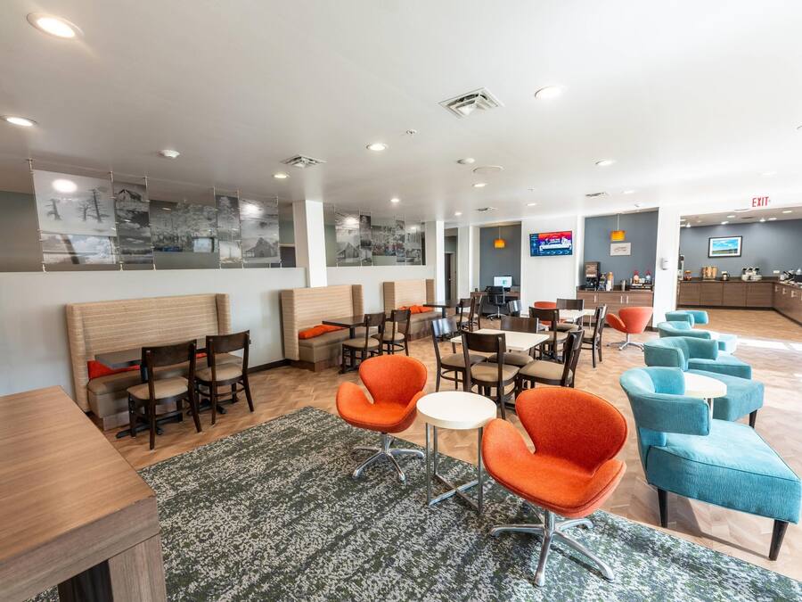 A modern hotel lobby with seating areas, a reception desk, and a large TV screen.