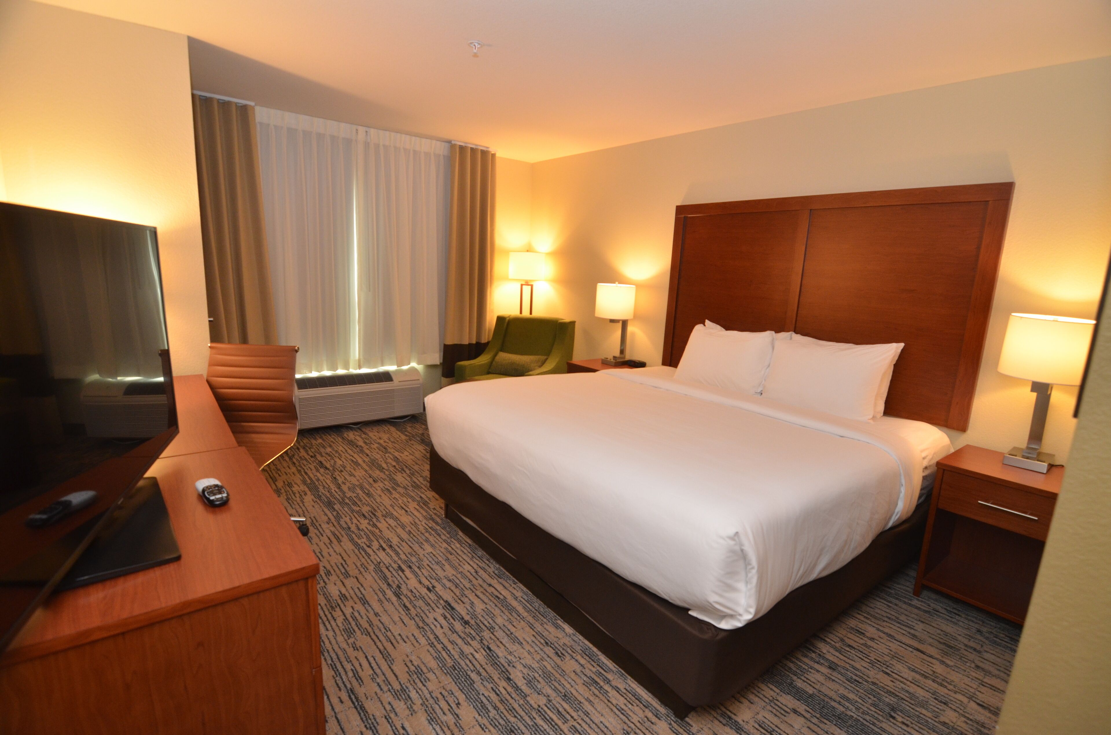 A hotel room with a large bed, a desk with a chair, a TV, and two bedside lamps.