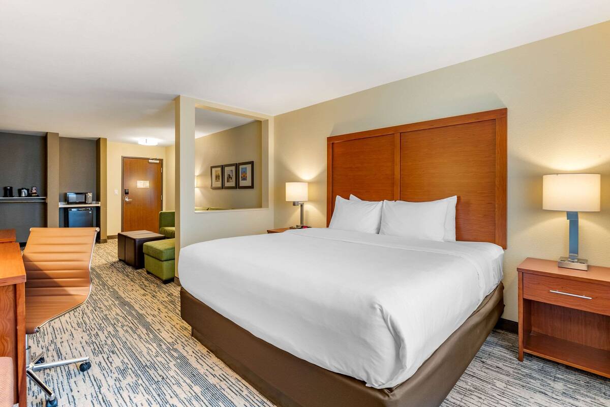 A hotel room with a large bed, a desk, a chair, a small table, a microwave, and a coffee machine.