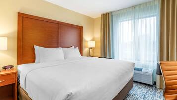 A hotel room with a large bed, wooden headboard, two bedside tables with lamps, a window with curtains, and a brown leather chair.