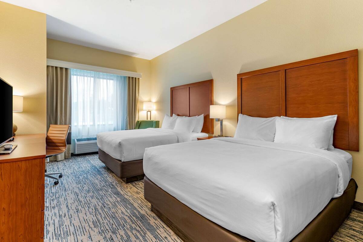 A hotel room with two beds, a desk, a chair, and a TV.