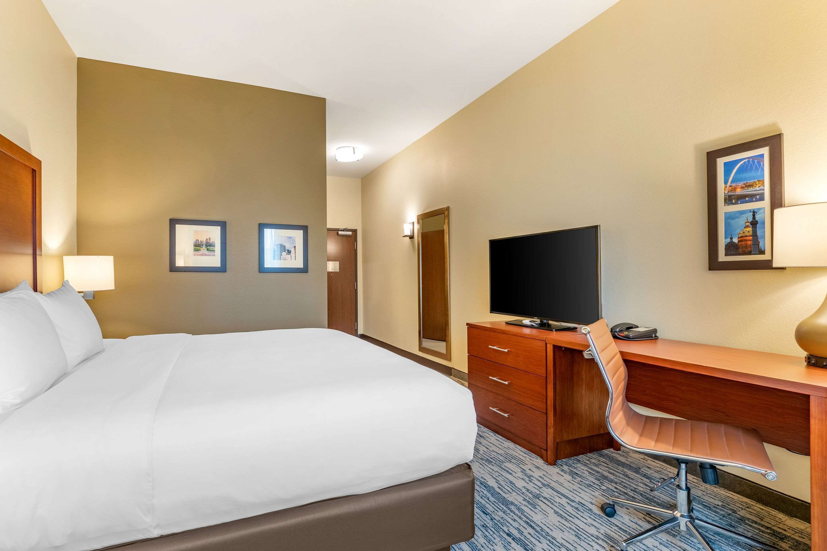 A hotel room with a large bed, a wooden desk, a chair, a television, and framed pictures on the wall.