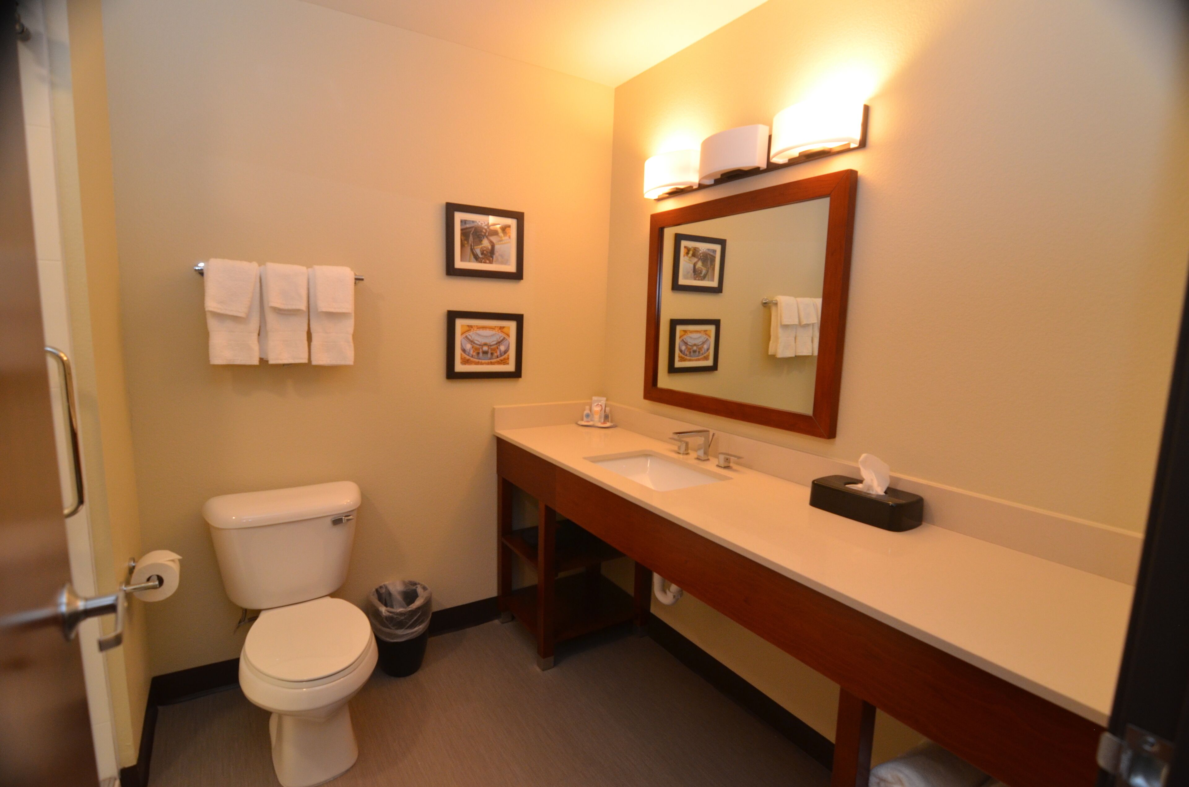 A bathroom with a toilet, sink, and mirror. There are towels hanging on the wall and a trash can.