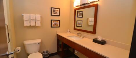 A bathroom with a toilet, sink, and mirror. There are towels hanging on the wall and a trash can.