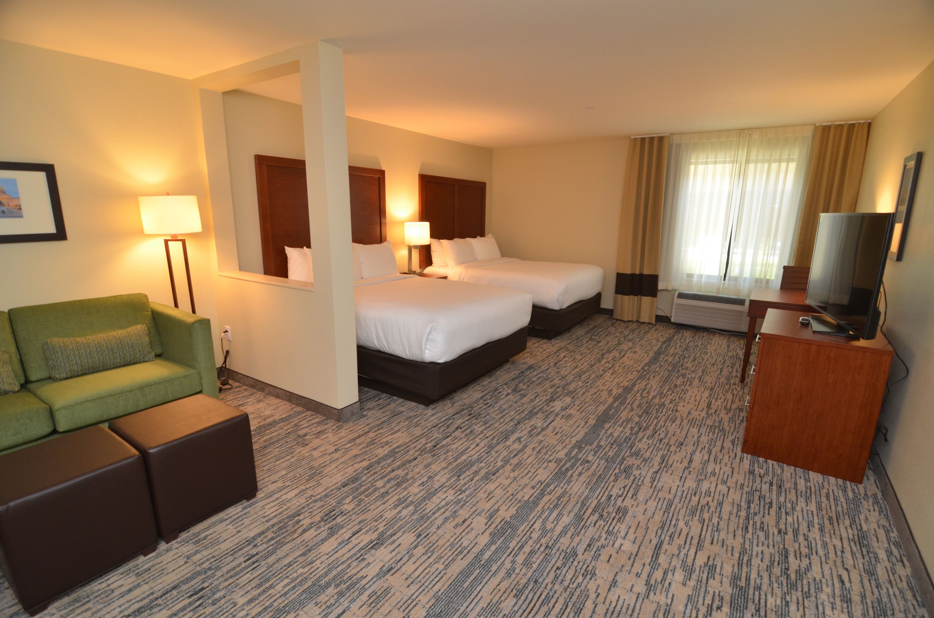 Habitación de hotel con dos camas, un sofá verde, un escritorio de madera y un televisor.