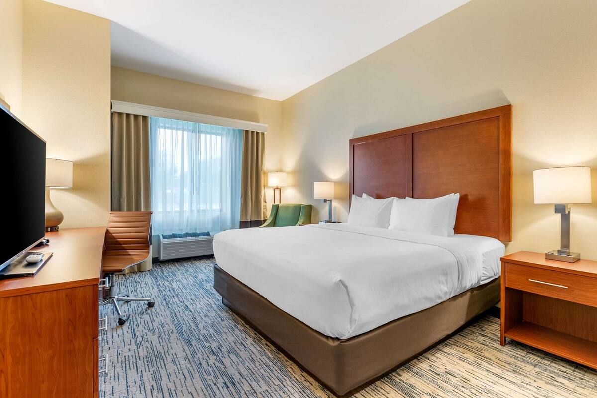 A hotel room with a large bed, a desk with a computer, a TV, and a chair.