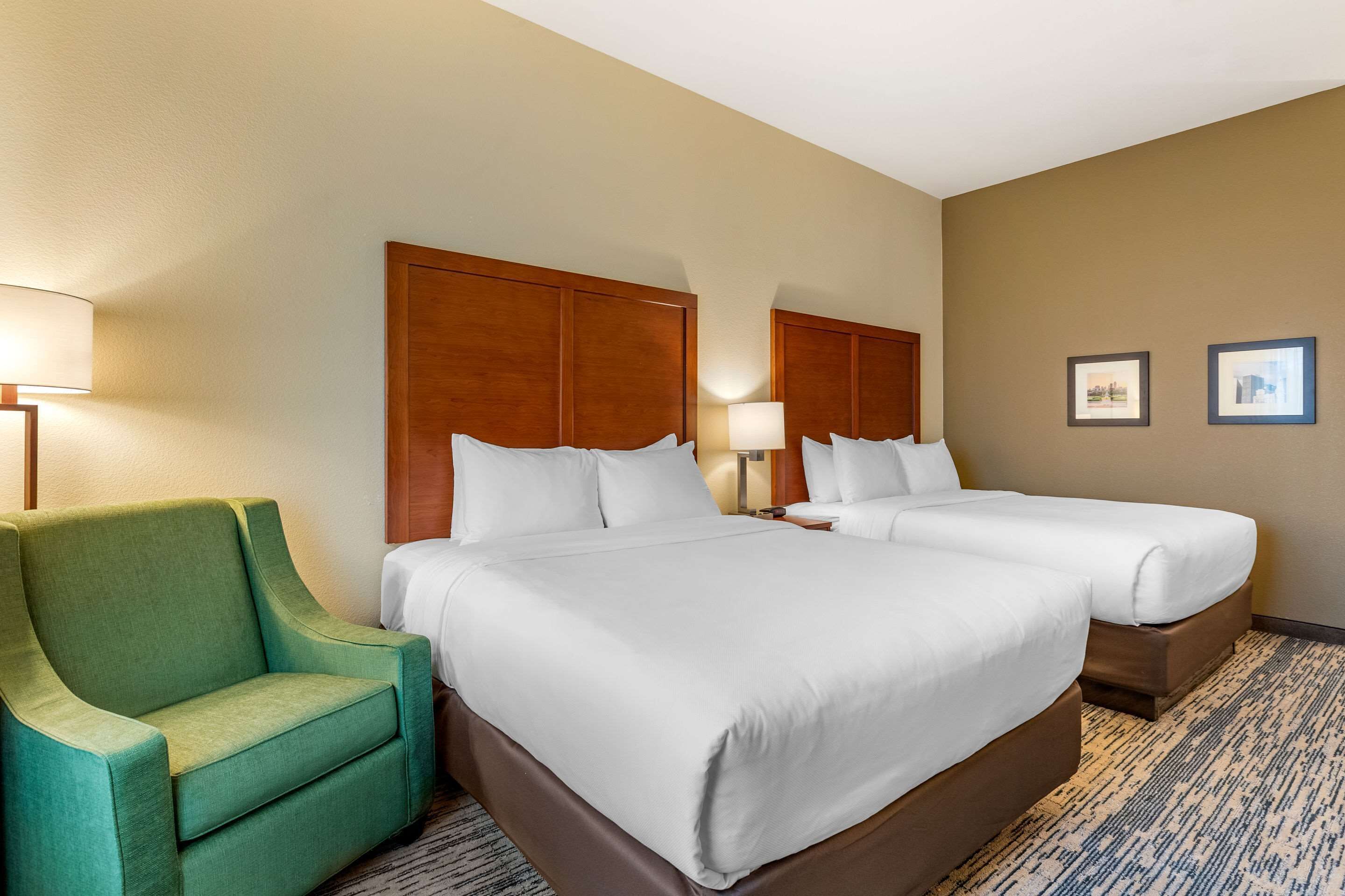A hotel room with two beds, a green armchair, and a carpeted floor.