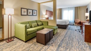 A hotel room with a green sofa, a bed, a desk, and a large mirror. - Comfort Inn & Suites West Des Moines (West Des Moines)