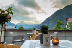 A terrace with a table and chairs, a candle, a menu board, and a view of mountains. - Wally Berg Apartements (Zams)